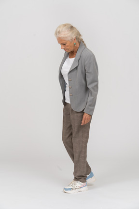 Вид сбоку на старушку в костюме, стоящую с руками в карманах