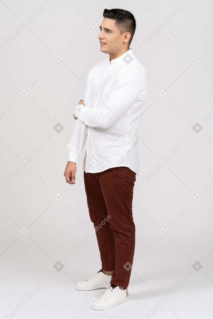 Vista de tres cuartos de un joven latino sosteniendo su codo y sonriendo con incertidumbre