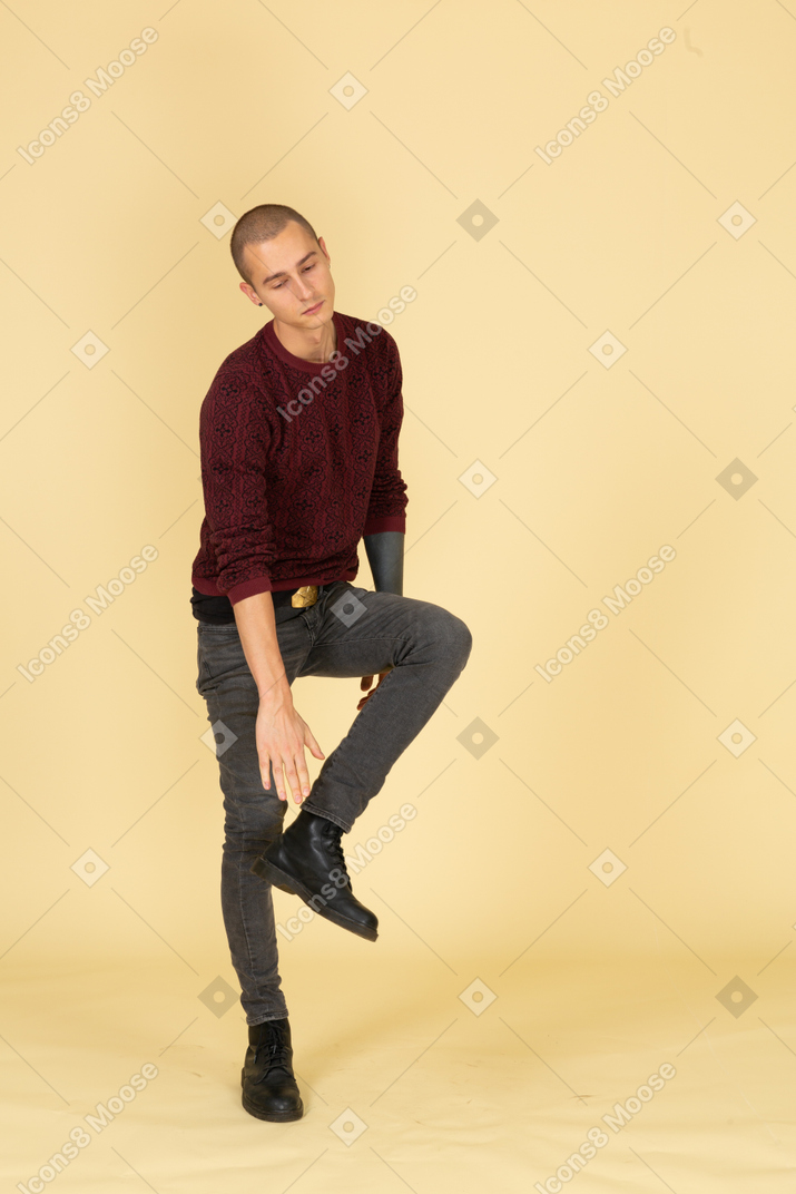 Vista de três quartos de um jovem cansado de pulôver vermelho tocando seu tornozelo