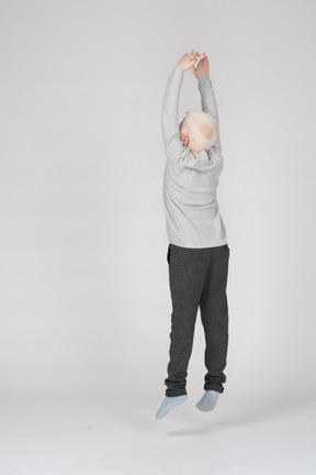 Vista posteriore di tre quarti di un ragazzo che salta con le mani in aria
