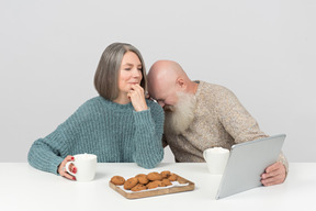 Aged man laughing hard while he and his wife watching movie on tablet