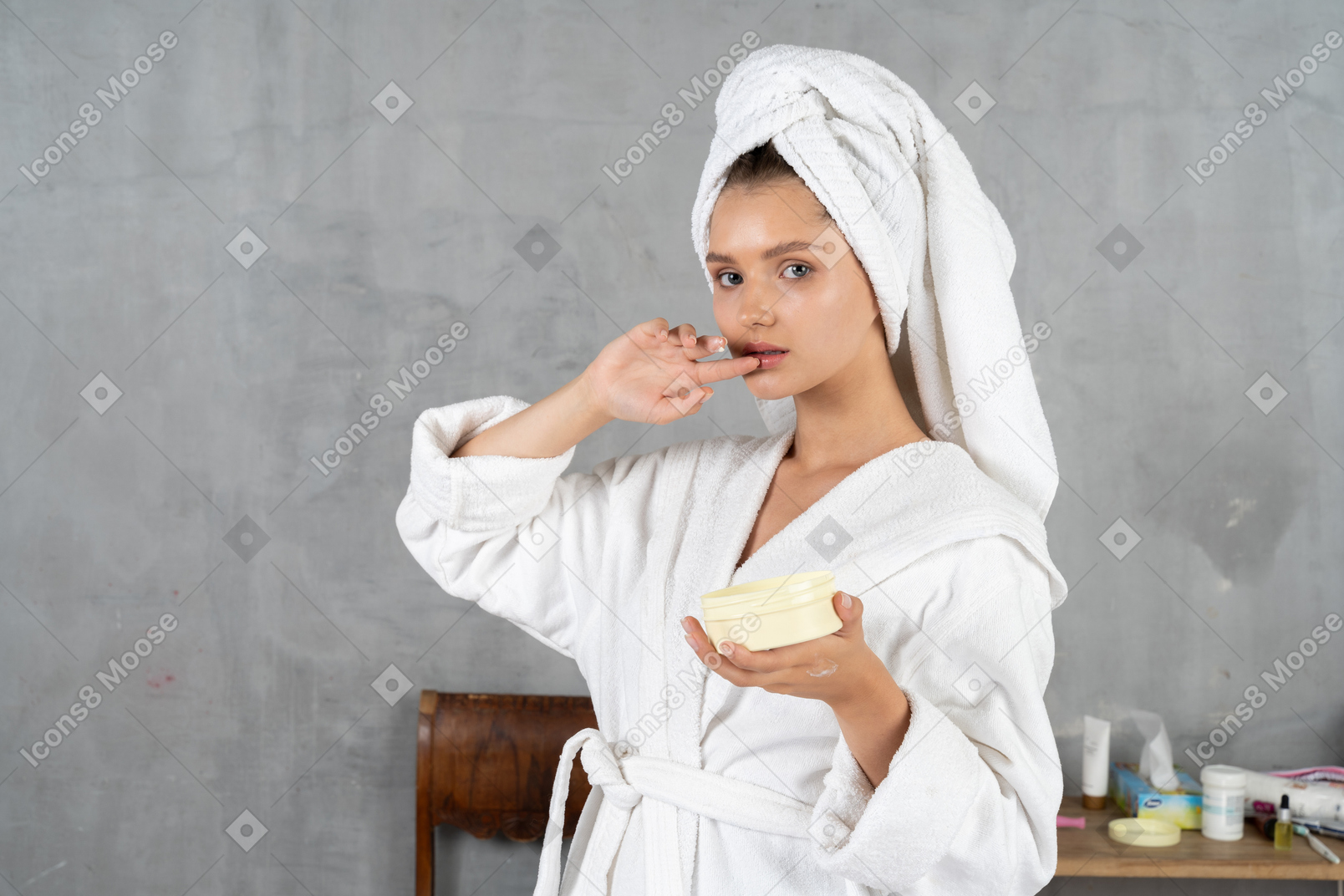 Woman in bathrobe touching lip and holding tub of cream
