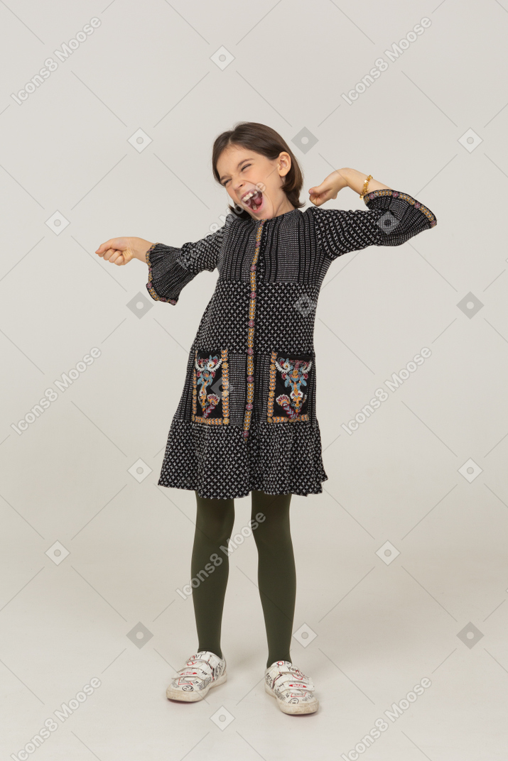 Vista frontale di una bambina che sbadiglia in abito allargando le braccia