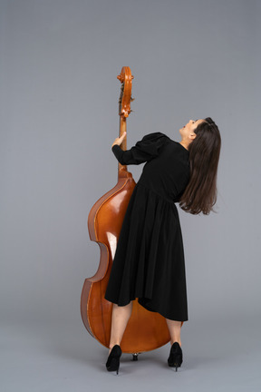 Vista de trás de uma jovem musicista vestida de preto segurando seu contrabaixo