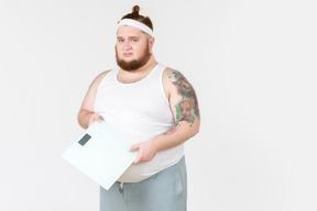 Sad young big guy in sportswear holding weights