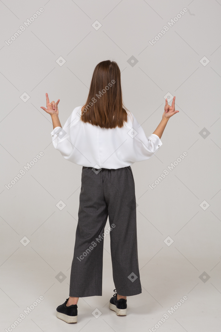 Back view of a young lady in office clothing showing rock gesture
