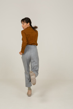Vista traseira de uma jovem mulher asiática correndo de calça e blusa