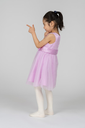 Menina asiática de vestido rosa apontando com uma arma de dedo