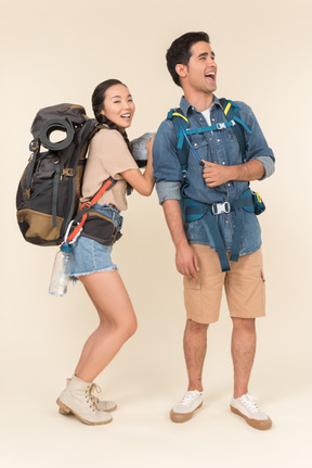 Laughing young asian woman taking something off from his boyfriend's backpack