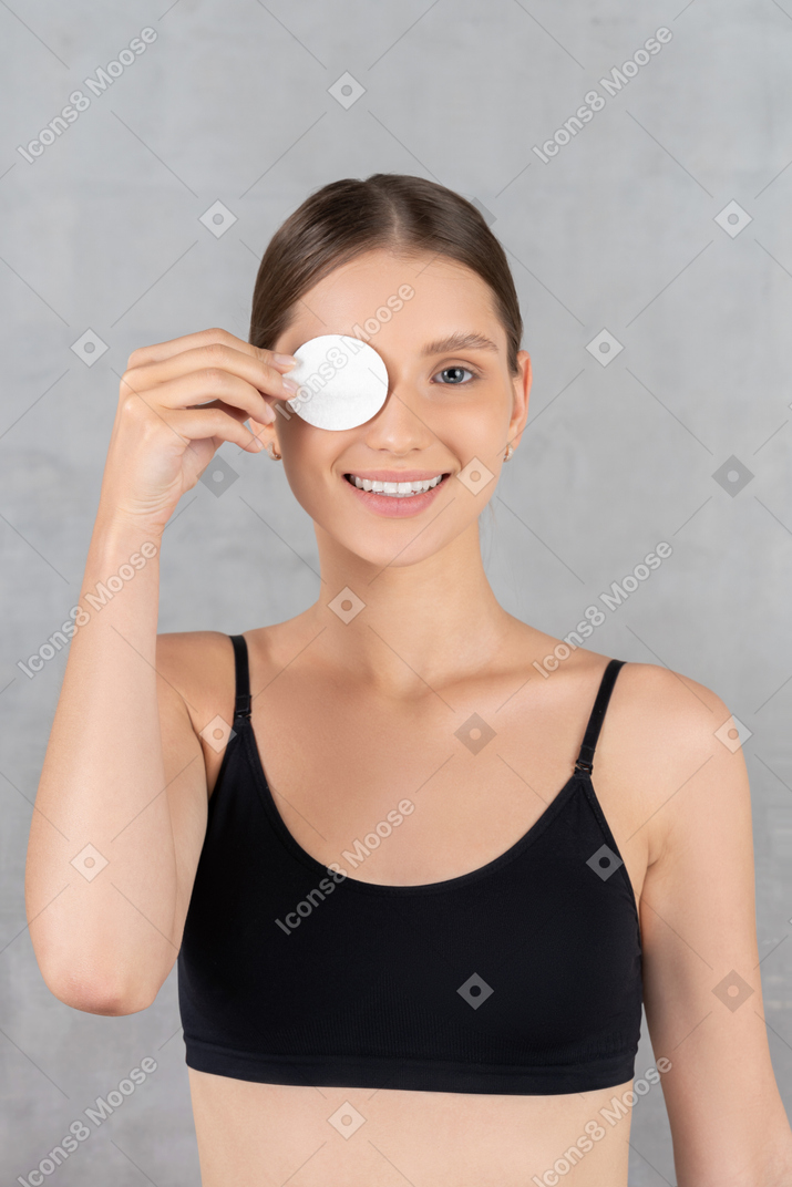 Mujer joven feliz que cubre el ojo con una almohadilla de algodón
