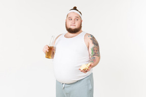 A fat man in sportswear holding a bottle of beer and offering chips