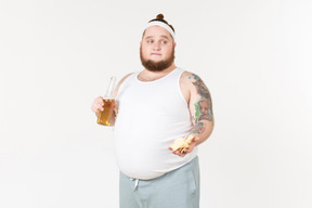 Um homem gordo em sportswear segurando uma garrafa de cerveja e oferecendo chips