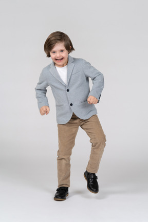 Cheerful young boy in jacket and pants dancing