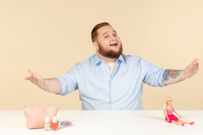 Rindo grande homem sentado à mesa com cosméticos e boneca barbie nele