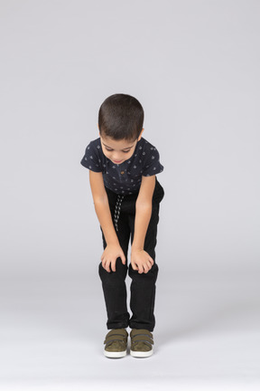 Vista frontal de um lindo garoto agachado e tocando os joelhos