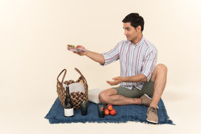 Young caucasian man sitting on the blanket and holding fruits
