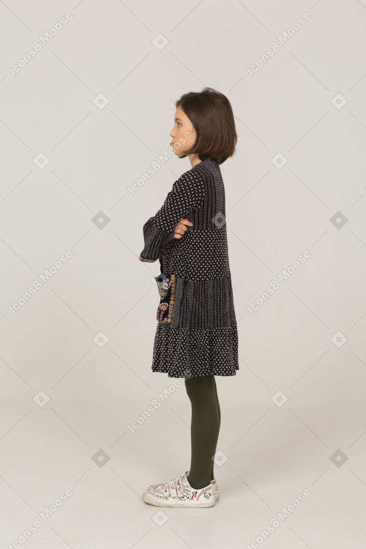 Vista laterale di una bambina imbronciata in abito che incrocia le braccia
