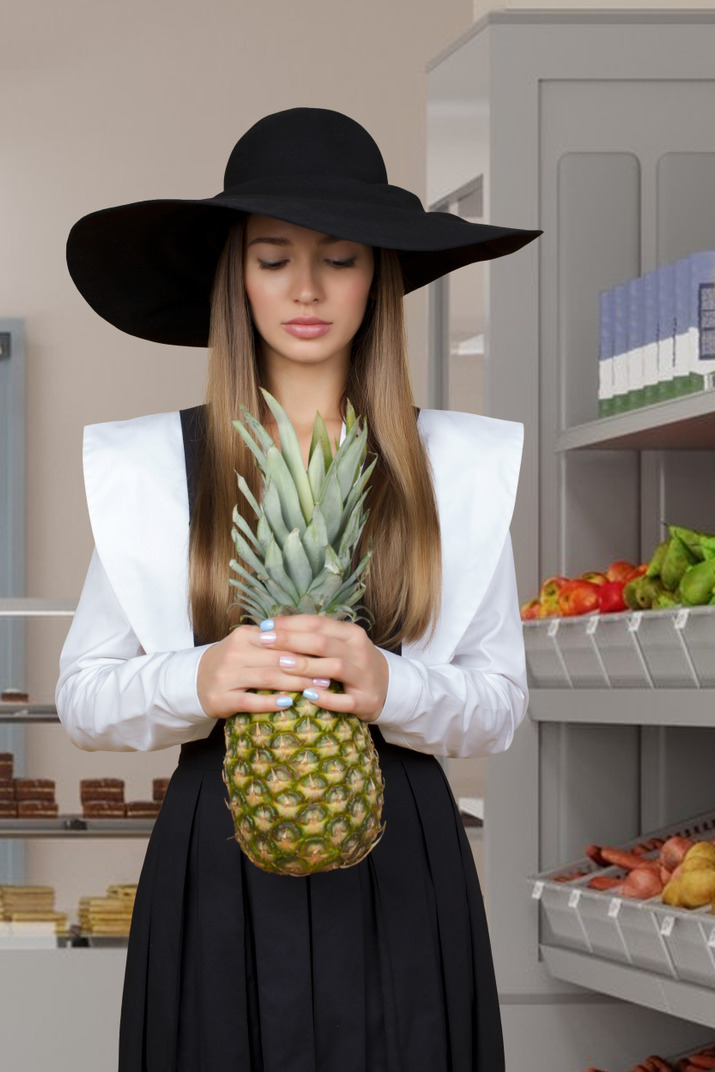 Young woman in a graduation cap and gown holding a pineapple
