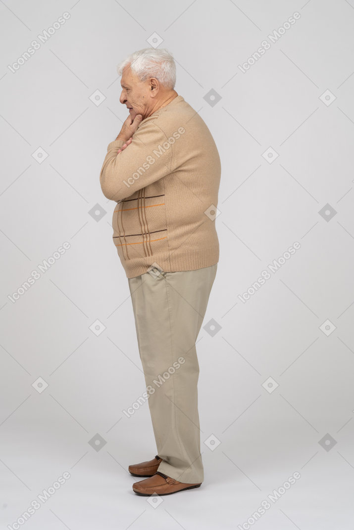 一位身穿休闲服、手放在下巴站着的体贴老人的侧视图