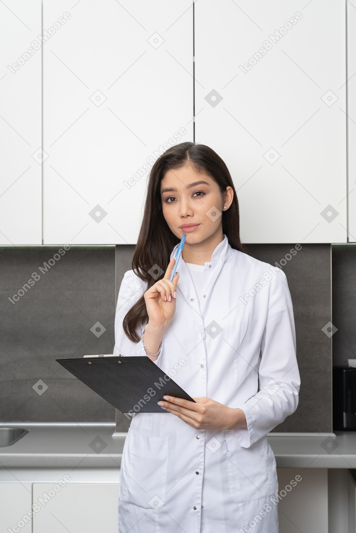 Front view of a serious female nurse holding a pen and a tablet while looking at camera