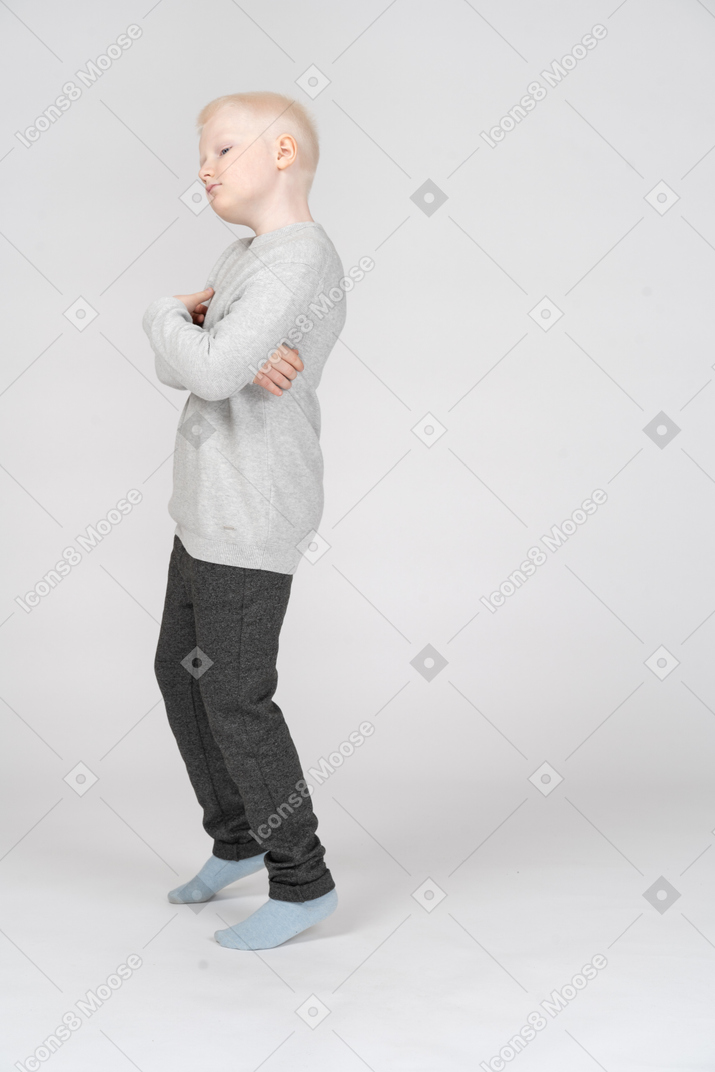 Side view of a naughty kid boy tilting head while crossing hands