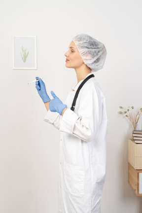 Side view of a young female doctor with stethoscope holding thermometer and showing thumb up