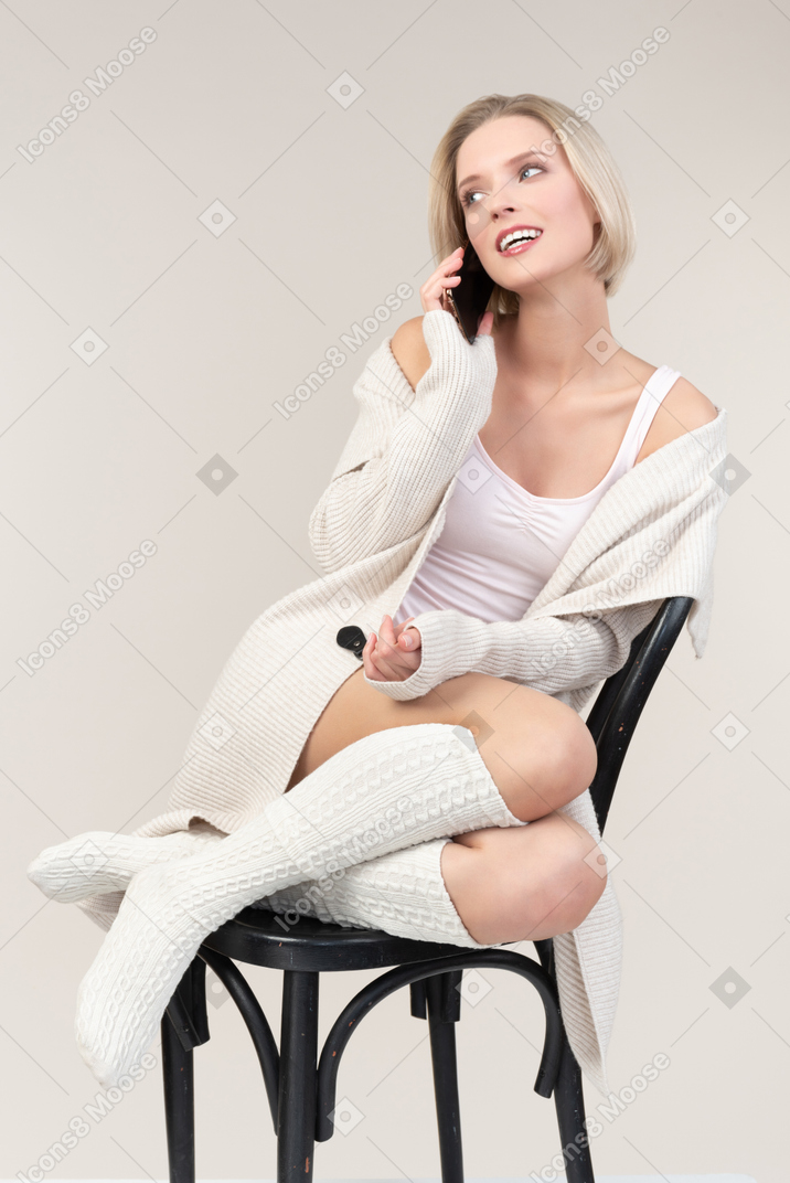 Pensive young woman sitting on chair and talking on the phone