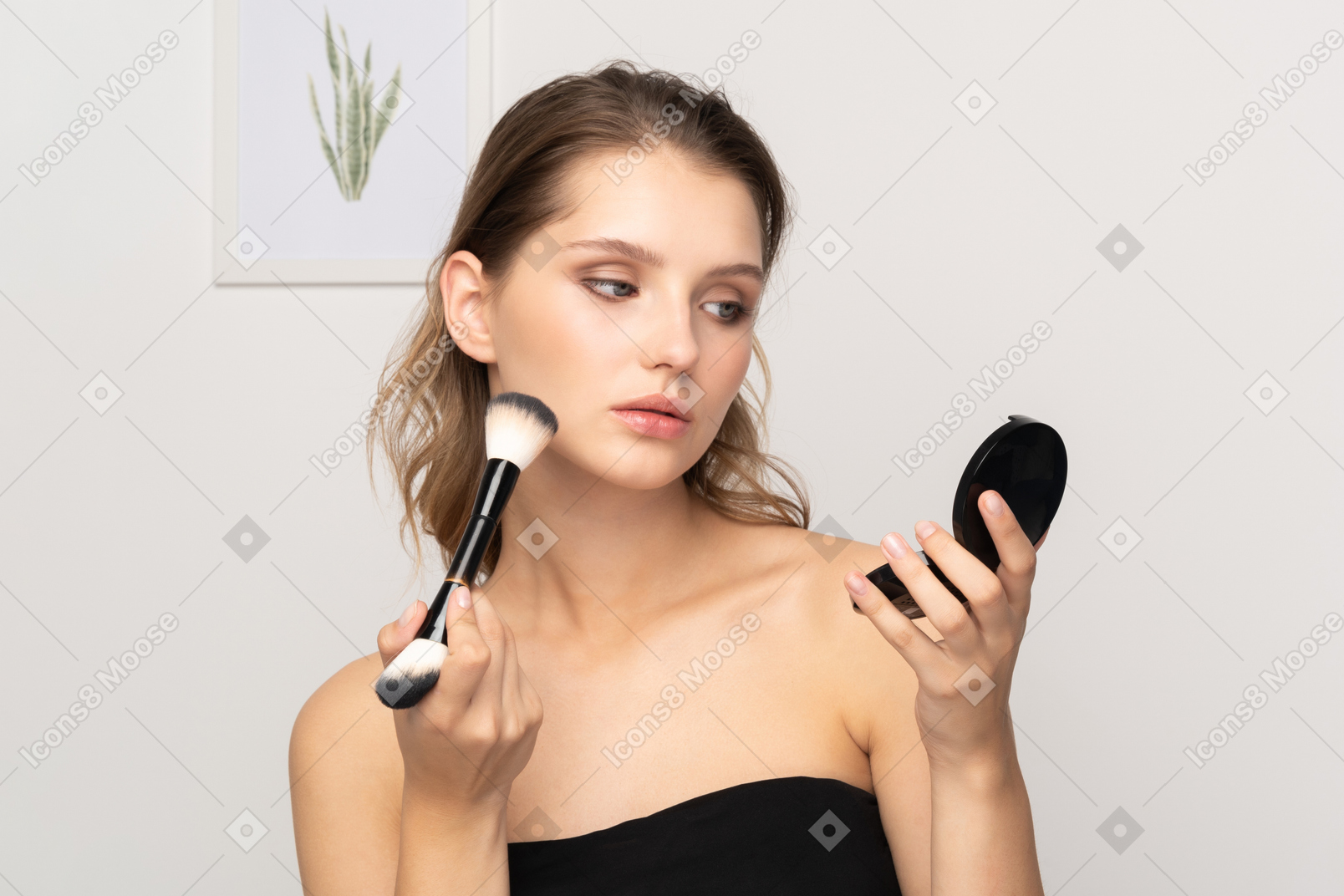 Front view of a young woman applying face powder while holding a mirror