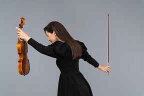Three-quarter back view of a female violin player in black dress making a bow