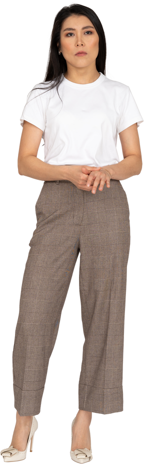 Vista frontale di una giovane donna seria in calzoni e maglietta che tengono le mani insieme