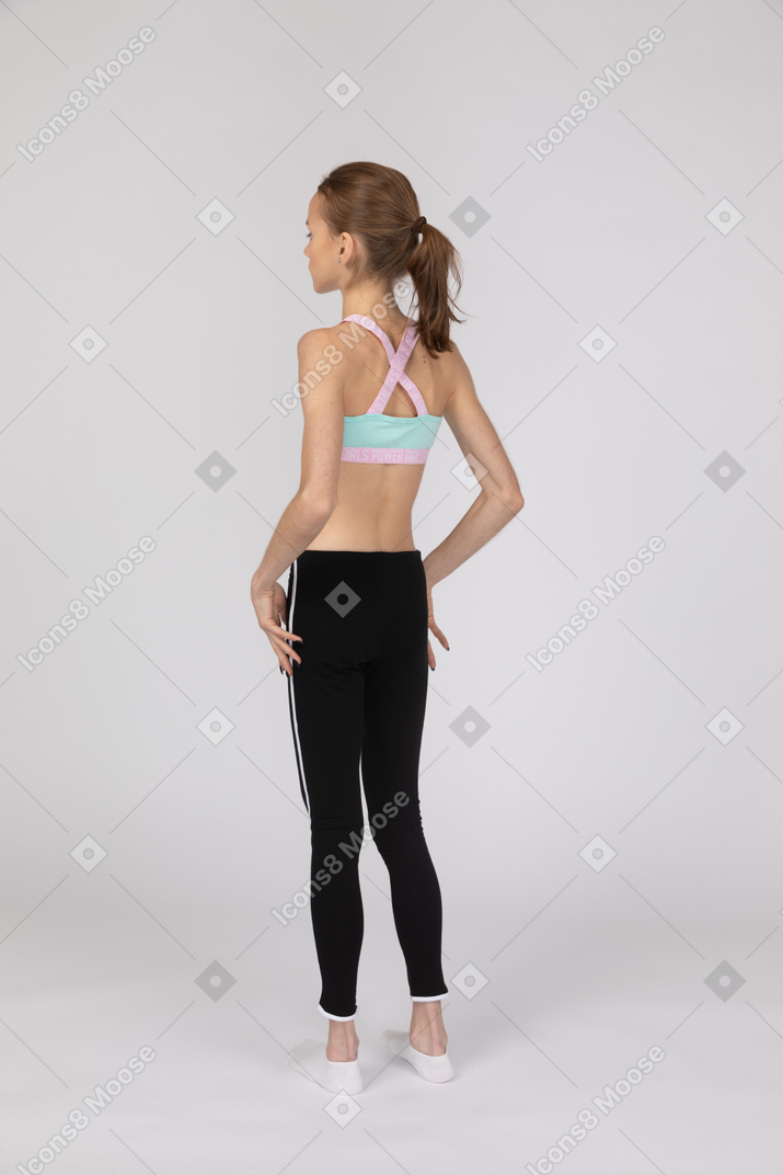 Vista posterior de tres cuartos de una jovencita en ropa deportiva tocando sus caderas
