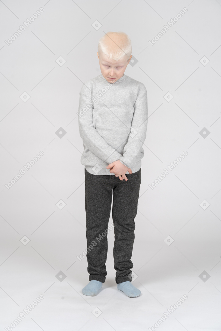 Vista frontal de un niño chico triste y avergonzado mirando hacia abajo