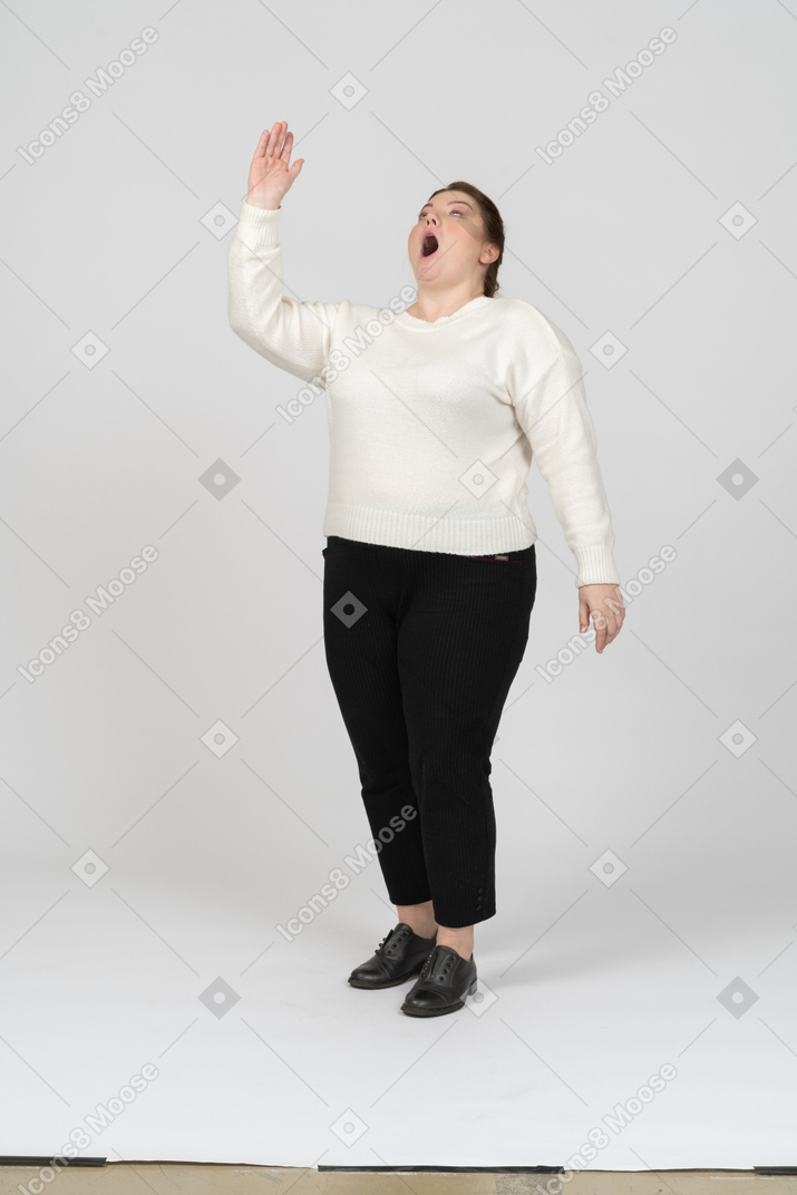 Вид спереди впечатленной женщины больших размеров в повседневной одежде, указывающей вверх рукой
