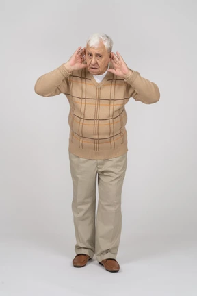Vista frontal de un anciano con ropa informal sostiene las manos cerca de las orejas