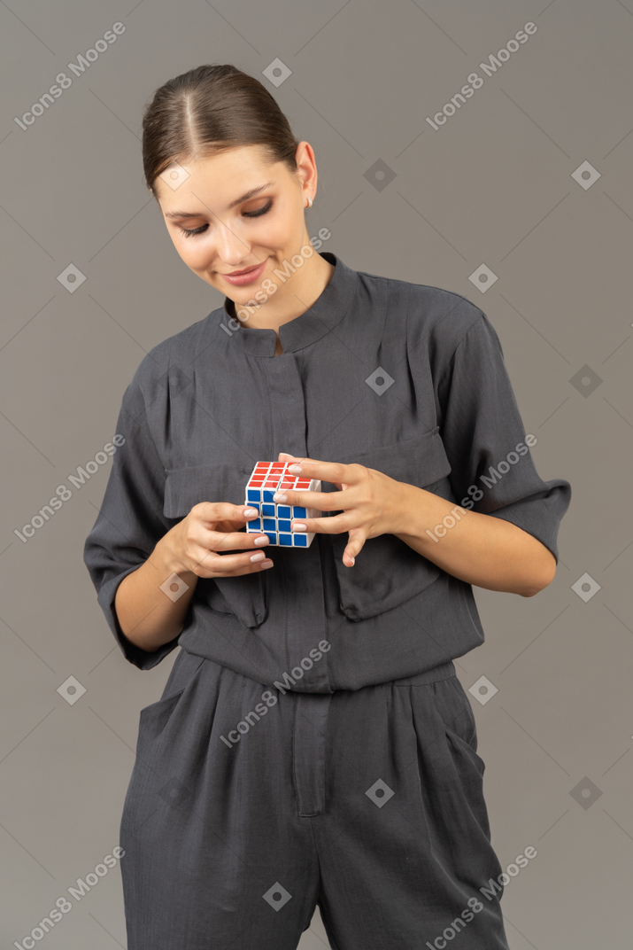ルービックキューブを保持しているジャンプスーツの笑顔の若い女性の正面図