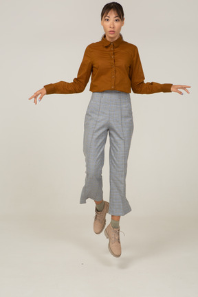 Front view of a jumping young asian female in breeches and blouse outspreading hands
