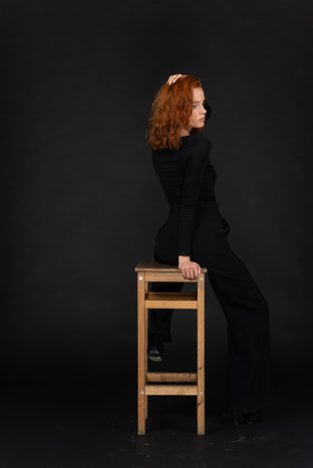 A back side view of the beautiful young woman sitting on the high wooden chair and adjusting her hair