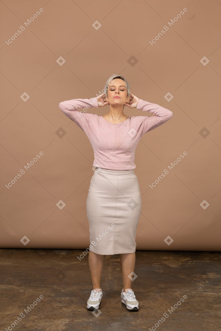 Vista frontal de una mujer en ropa casual de pie con las manos detrás de la cabeza