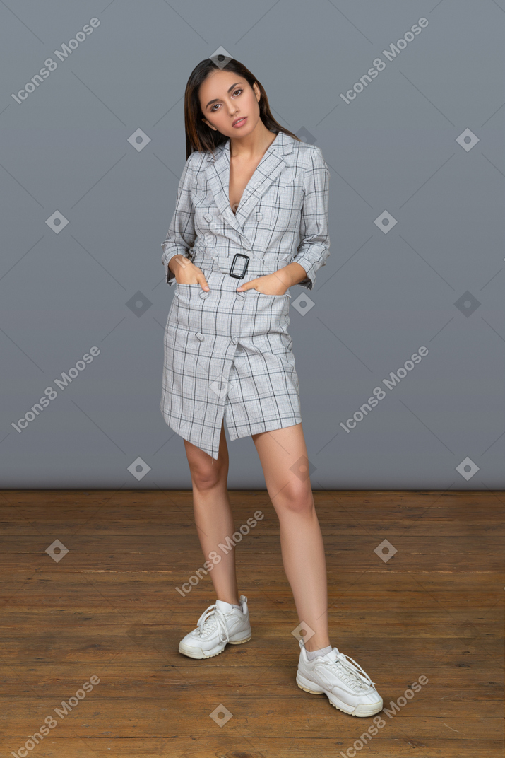 Emotionless young woman keeping hands in pockets while facing camera