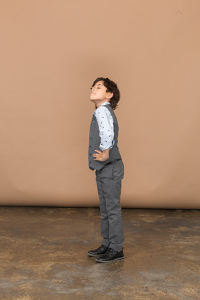 一个穿着灰色西装的可爱男孩双手叉腰站着抬头仰望的侧视图