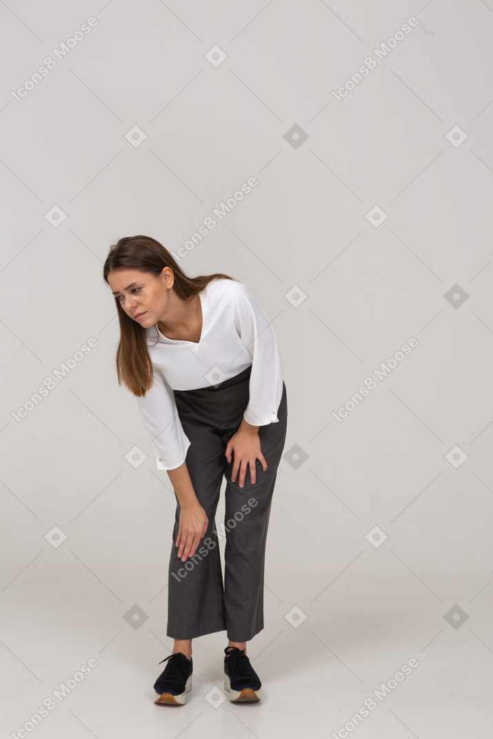 Front view of a young lady in office clothing bending down & touching knee
