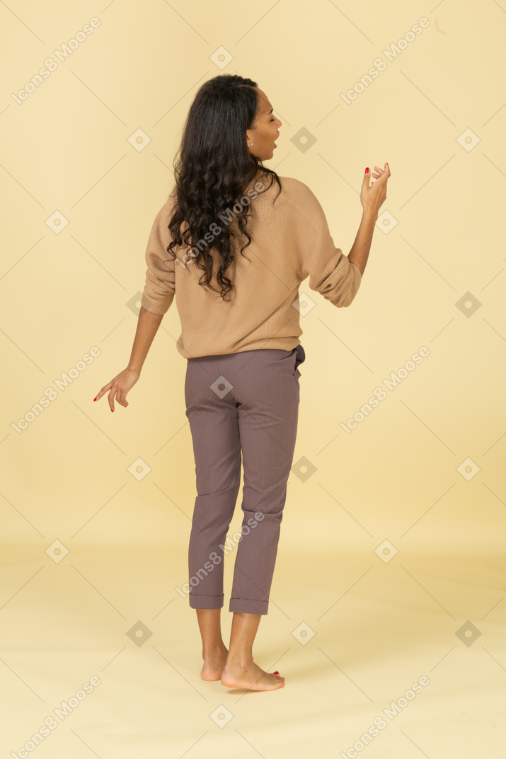 Vista posterior de una mujer joven de piel oscura que habla levantando su mano