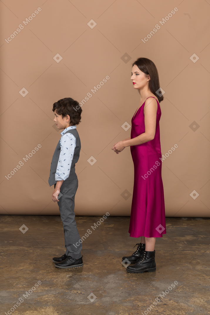 站立和握她的手的礼服的少妇与男孩