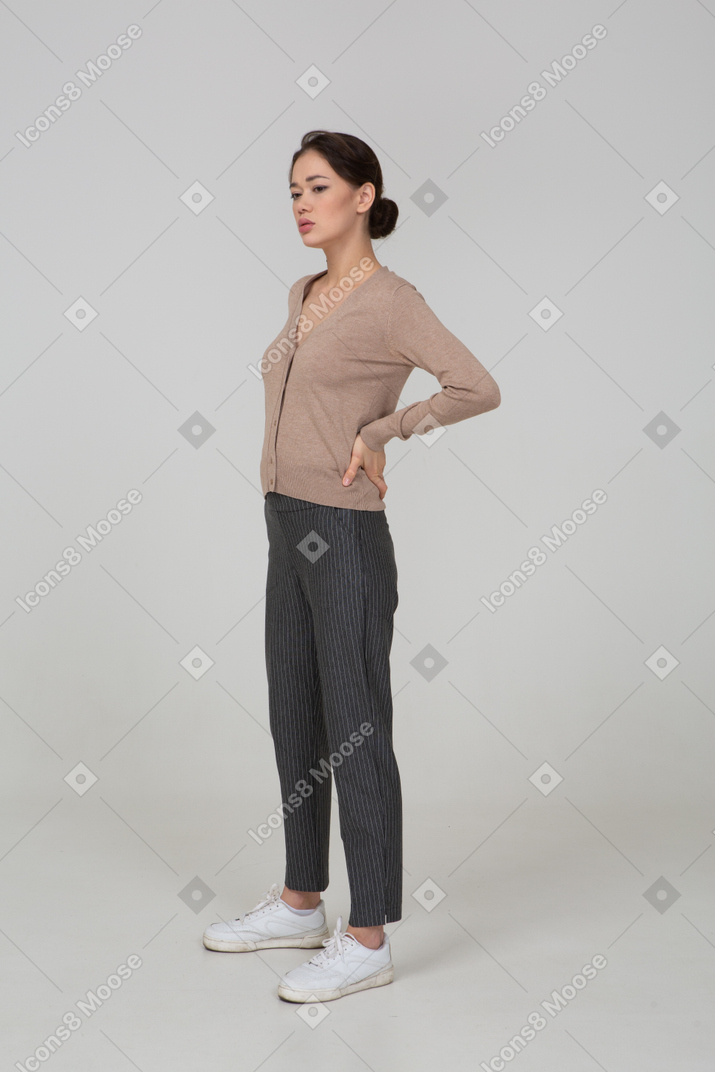Вид в три четверти молодой женщины в пуловере, положившей руки на бедра и штаны, смотрящей вниз
