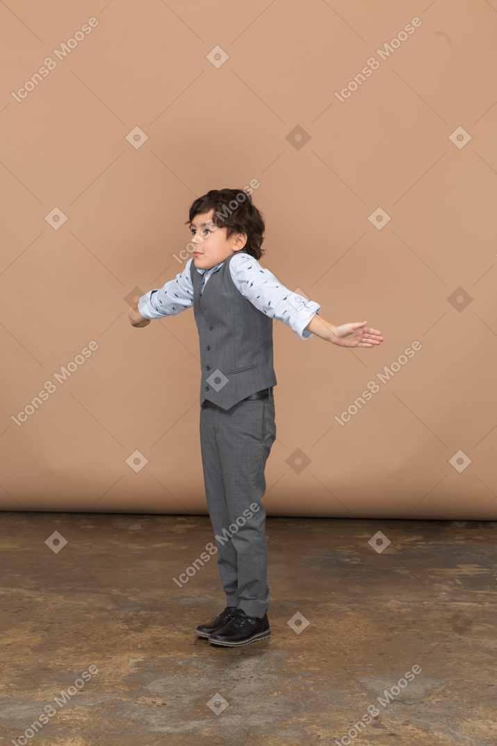 Side view of a boy in suit standing with outstretched arms