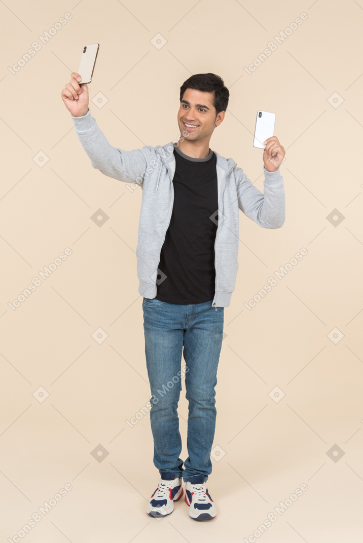 Laughing young caucasian man holding two smartphones