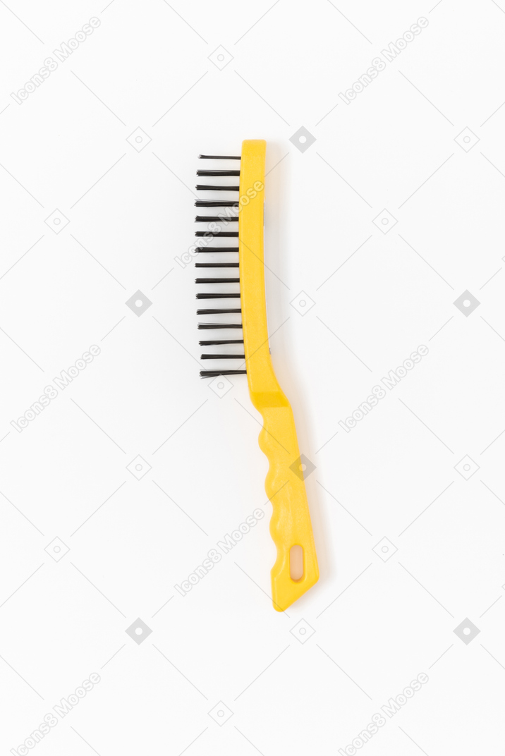 A steel wire brush with a bright yellow handle lying on the plain white background