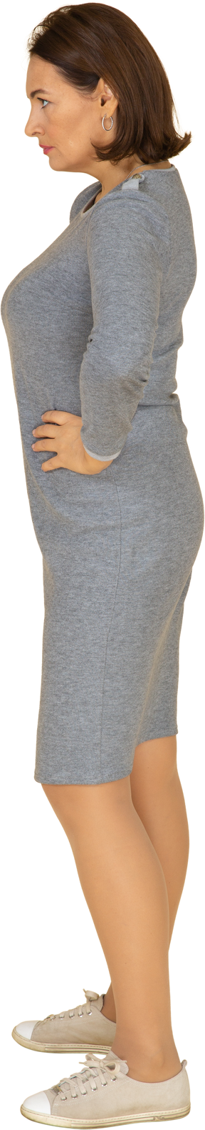Vista lateral de uma mulher com vestido cinza em pé com as mãos na cintura