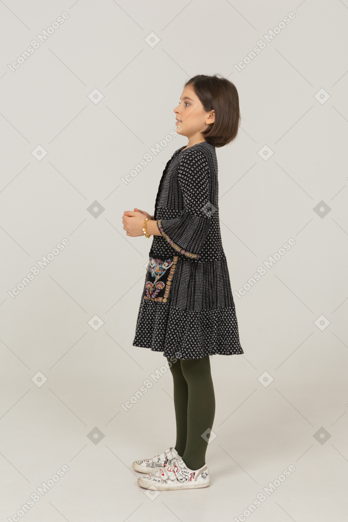 Side view of a confused little girl in dress holding hands together