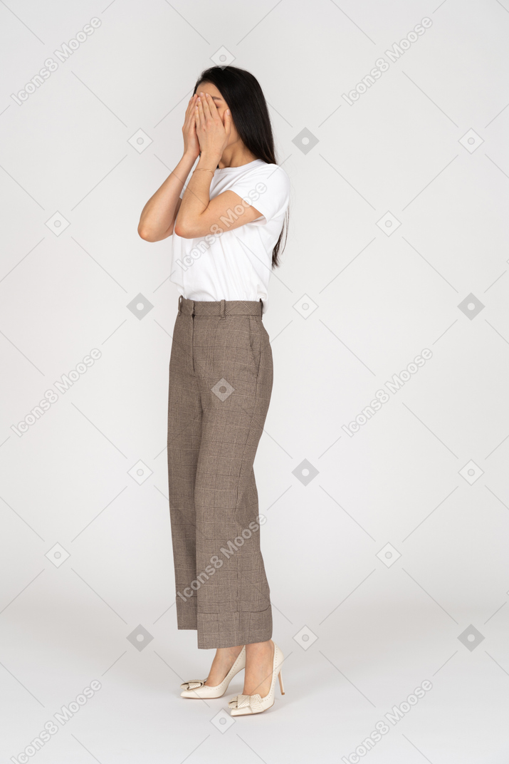 Three-quarter view of a young lady in breeches and t-shirt hiding her face